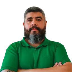 Portrait of a man with a grey-streaked beard, arms crossed, wearing a green polo shirt